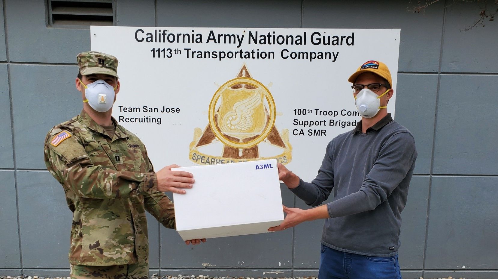 ASML employee handing box of face masks to member of California National Guard