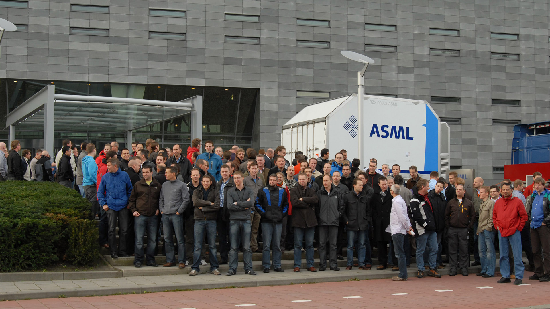 一群员工站在荷兰Veldhoven的ASML总部面前，庆祝2010年首款EUV机器发货。