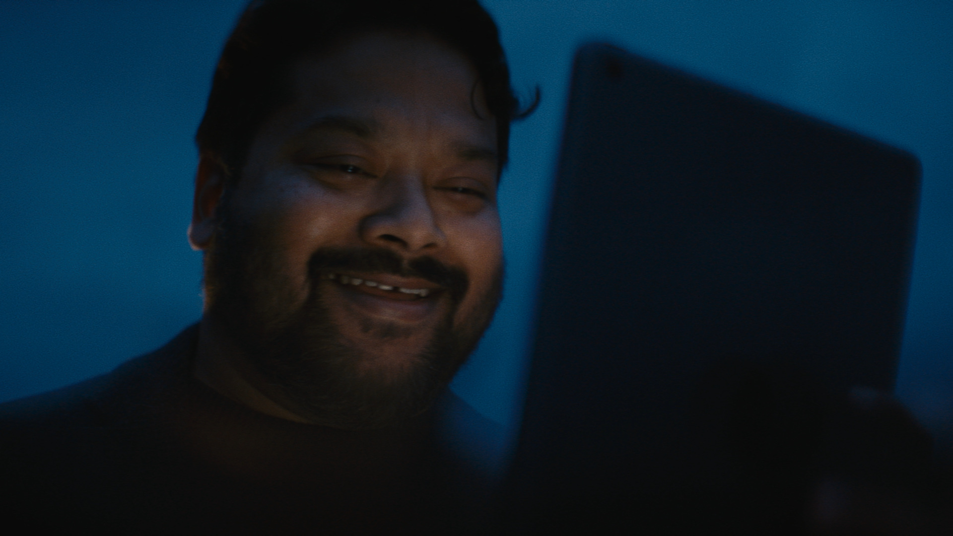 一个人微笑,他看着一个平板电脑,照亮了他的脸。